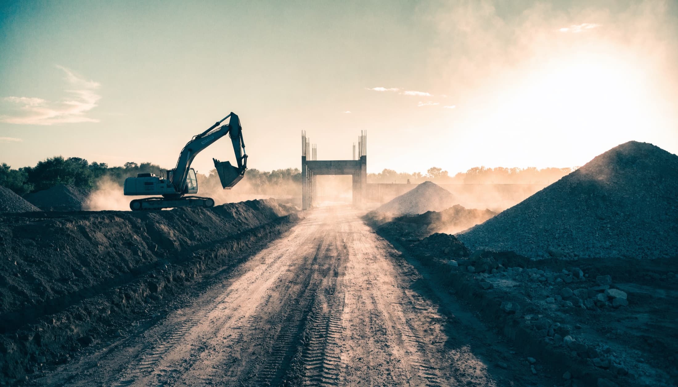 An excavator working beside a haul road leading to a concrete structure on a UK civil engineering site at golden hour